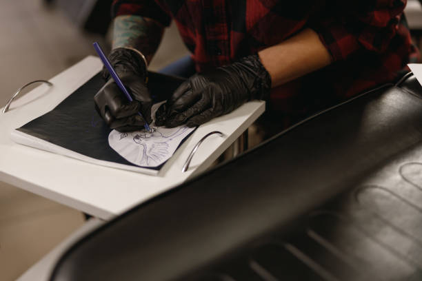istock Tattoo master in black gloves drawing picture for client 1386537700