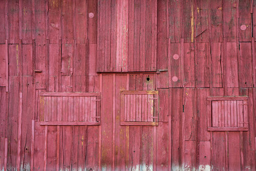wall of old, wooden, weathered red painted barn - rustic wood background and texture with multiple doors and windows