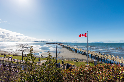 People walking on white rock pier with Canada flag in the foreground.