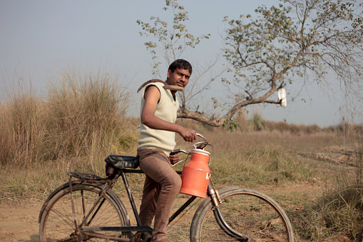 Rural farmer of Indian ethnicity riding cycle in the field holding sickle on the shoulder outdoor in the field portrait outdoor in nature.