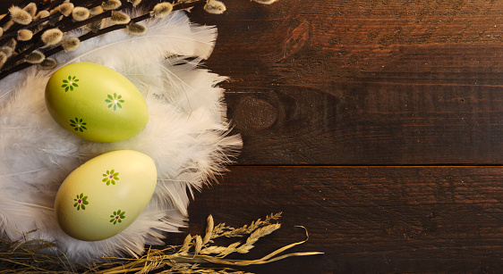 Easter eggs with feathers, pussy willow, straw on a rustic wooden background and warm light