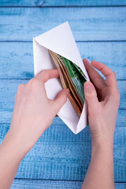 istock Hands holding an open envelope with money on a blue background 1386561770