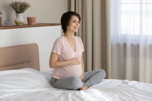 cute pregnant woman laughing sitting on king size bed - labour room imagens e fotografias de stock