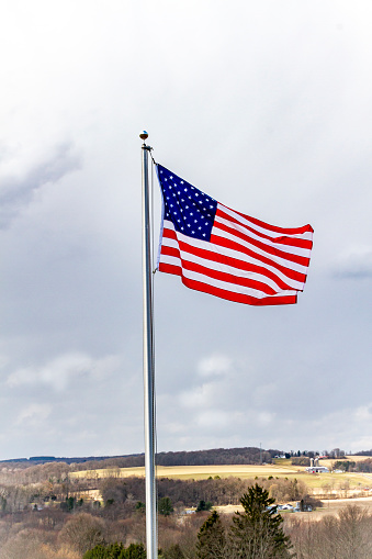 American flag with cloudy sky and farm s in the background