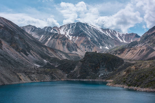 istock Deep mountain lake of phantom blue color among sharp rocks and high mountains in changeable weather. Wonderful dramatic view to deep blue mountain lake and large sunlit rocky cliff under cloudy sky. 1386577837