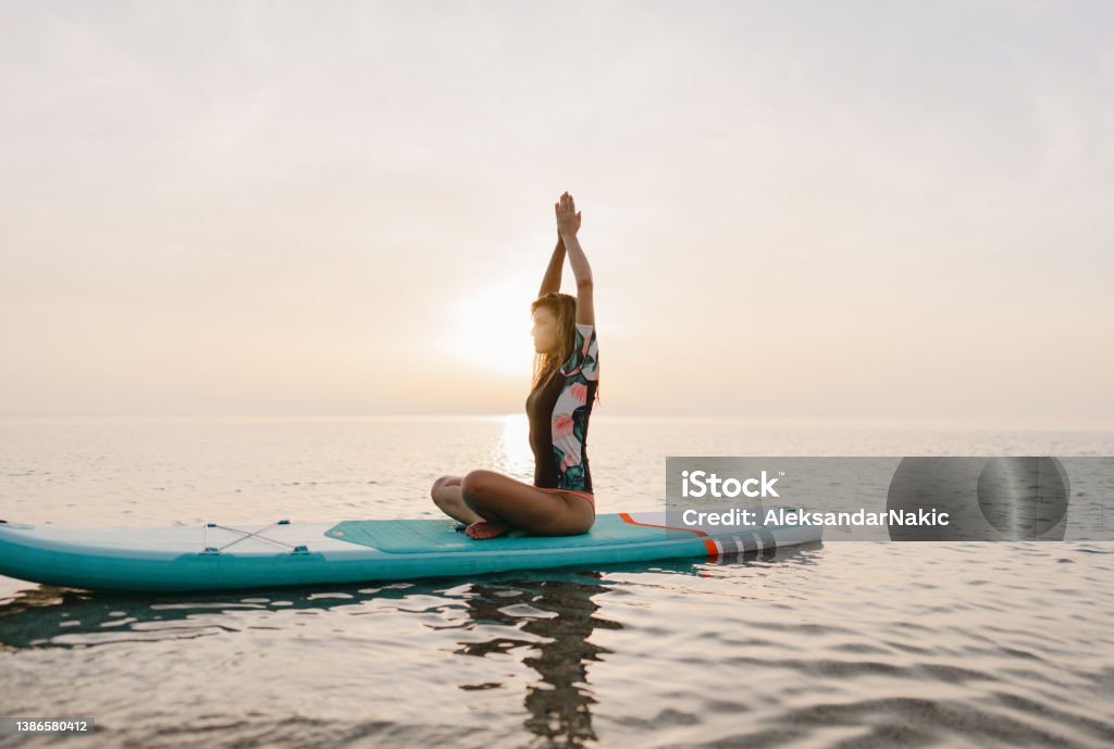 Meditating on a paddle board Photo of a young woman practicing yoga and meditation on a paddleboard. Yoga Stock Photo