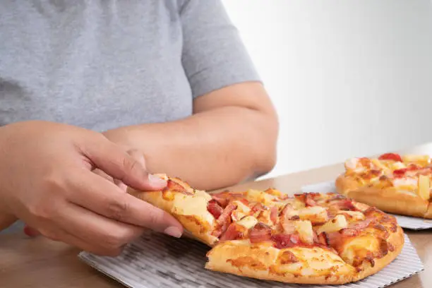 Hungry overweight woman holding Pizza And happy to eat pizza. Concept of binge eating disorder (BED) and Relaxing with Eating junk food and unhealthy foods.