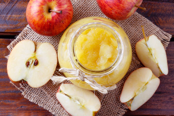 homemade apple sauce or apple puree in glass bowl over rustic wooden table homemade apple sauce or apple puree in glass bowl over rustic wooden table. top view apple compote stock pictures, royalty-free photos & images