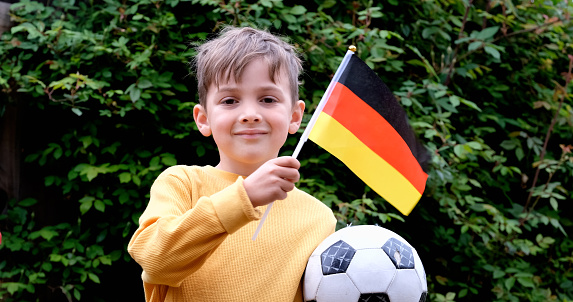 Smiling caucasian boy waving a German flag holding a soccer ball looking at the camera
