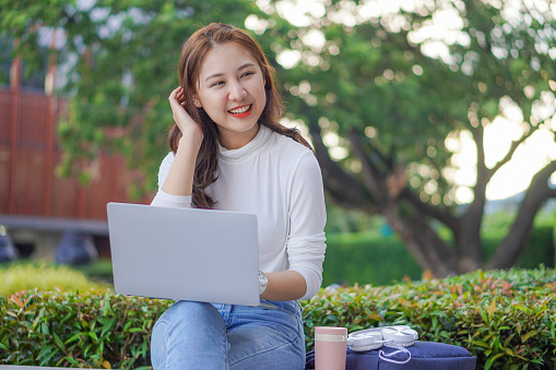 Asian woman publicly uses their laptop to study and work outdoors in shopping malls.