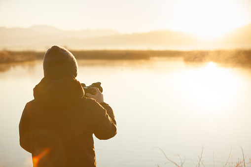 silhouette of photographer taking pictures of sunrise over lake