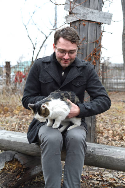 istock Young man sitting on a bench and petting a cat 1386617190