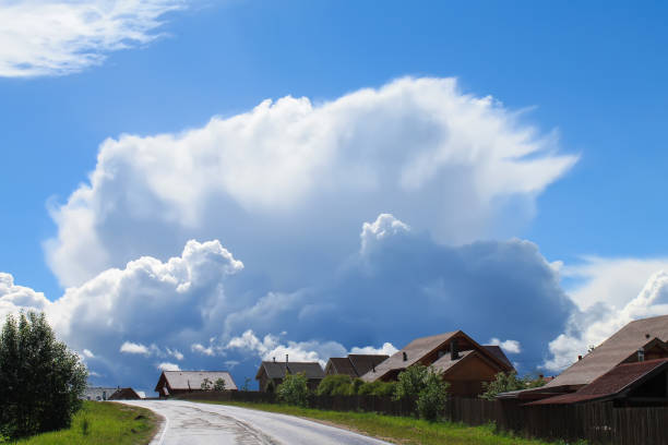 Large huge cumulus white clouds rise above European village road after rain wet with evaporation blue sky
