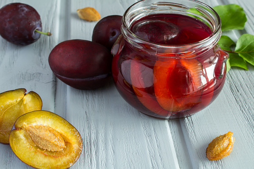 Compote of plums in the glass jar on the gray wooden background. Close-up.