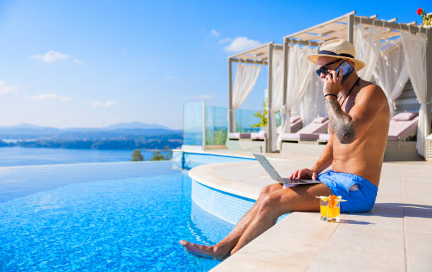 休暇中に仕事をしている男性、電話で話したり、プールサイドでラップトップコンピュータを使用している男性 - on beach laptop working ストックフォトと画像