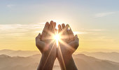 Human hands praying to god on mountain sunset background
