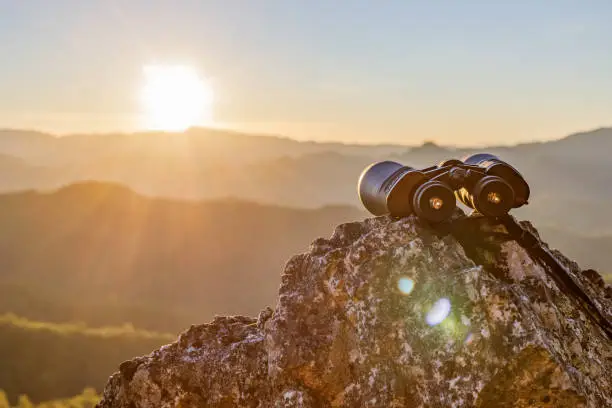 Photo of binoculars on top of rock mountain at beautiful sunset background.