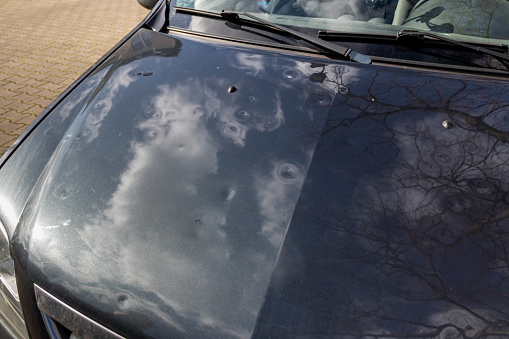 Car engine hood with many hail damage dents show the forces of nature and the importance of car insurance and a replacement value insurance against stormy weather and storm hazards or extreme weather