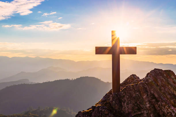 silhouetten des kruzifix-symbols mit hellem sonnenstrahl auf dem bunten himmelshintergrund - gods rays stock-fotos und bilder