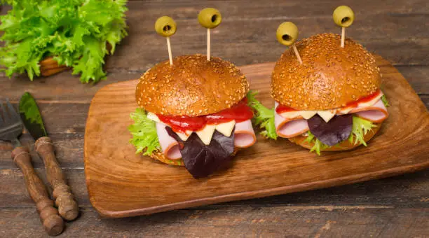 Photo of Monster hamburgers on wooden plate on brown background. Fun food art for kids. Fast food and junk food concept.