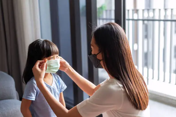 The shot of mother wearing mask setting the facemask of her cute child.
