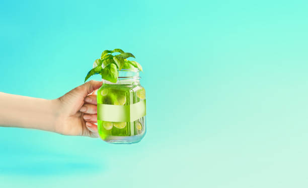 Green summer drink, lemonade with cucumber and lemon slices, flavored with herbs in Mason jar in women hand Green summer drink, lemonade with cucumber and lemon slices, flavored with herbs in Mason jar in female women hand at mint turquoise background. Summer mood. Healthy beverage. Infused water. mason jar lemonade stock pictures, royalty-free photos & images