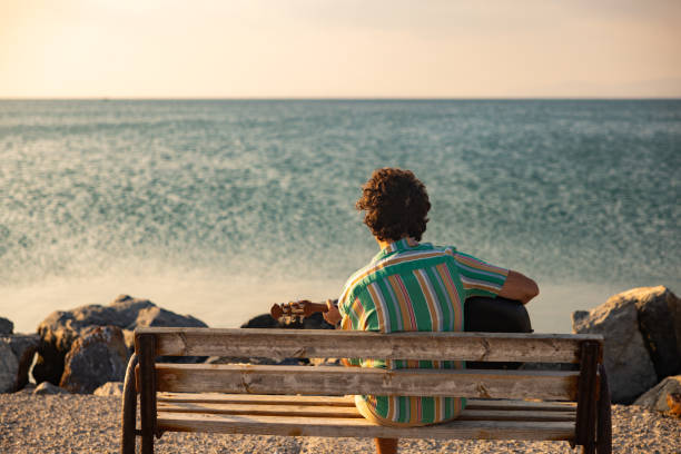 istock Young man sitting and playing guitar by the sea 1386670853