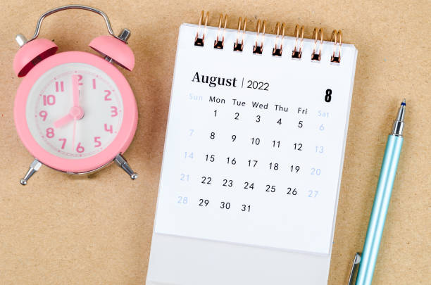 istock August 2022 Desk calendar with pink alarm clock on brown background. 1386672049