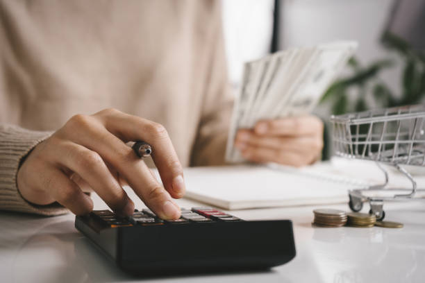 woman counting and calculate cost money with calculator at home. budget of disadvantaged and low income family for rising food and grocery store prices and expensive daily consumer goods concept. - inflation imagens e fotografias de stock