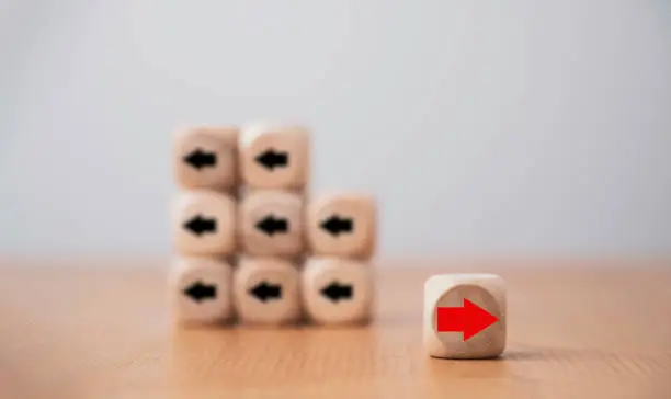 Photo of Red arrow on wooden move on different direction with black arrow on cube for business and technology disruption or unique concept.