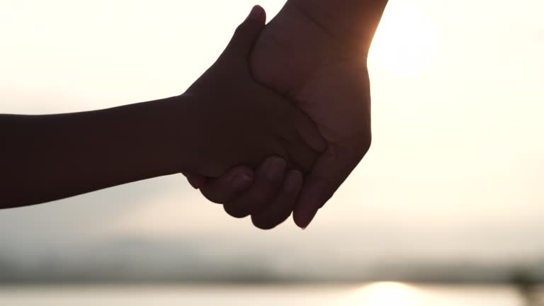 Happy Family, Mothers Day, Children's Day Concept. Mother and daughter hands joining and holding together and enjoying sunset flare in meadow nature background. Romantic moment mother and child girl.