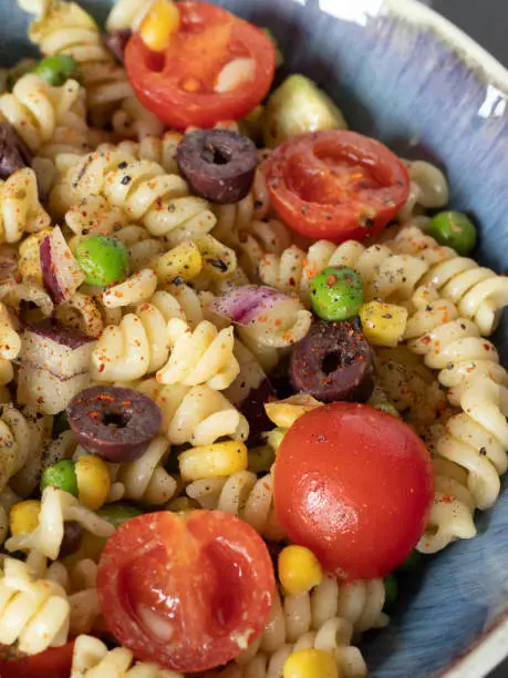 Plant-based vegan spicy pasta salad in a bowl made with fresh vegetables: cherry tomatoes, green peas, olives, and corn. A closeup. Eating healthy food concept.