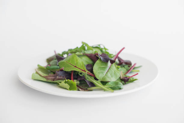 green leaves of spinach, arugula, lettuce in a white plate on a white table