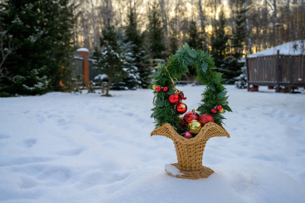 A bright Christmas basket with green branches and Christmas decorations stands on white snow against the backdrop of snowy nature. Sunny natural background