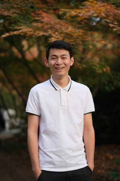 istock cheerful Asian young man looking at camera with blur maple tree 1386701877