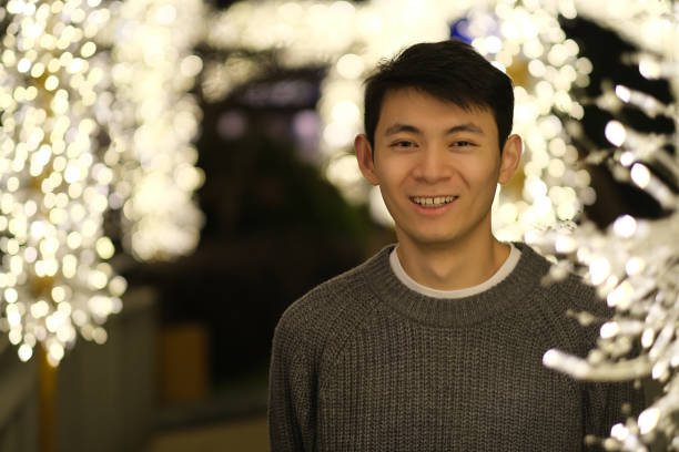 smiling Asian young man looking at camera at night with golden lights bokeh