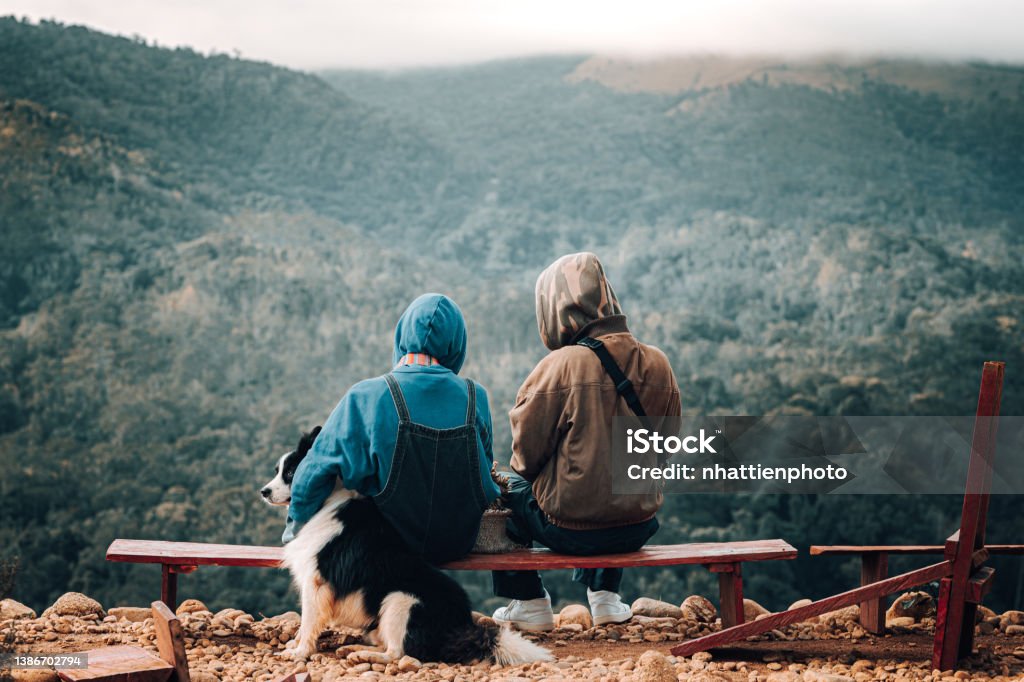 Relaxed Young Couple tourists admiring the view from the mountain top, with dog, camping concept stock photo Young couple go camping in Da Lat, Vietnam. With dog. Their backs are turned towards the camera and they are looking ahead at the scene. They are on vacation in Da Lat. Dalat Stock Photo