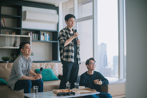 Asian Chinese male friends enjoying karaoke session at home during weekend eating pizza