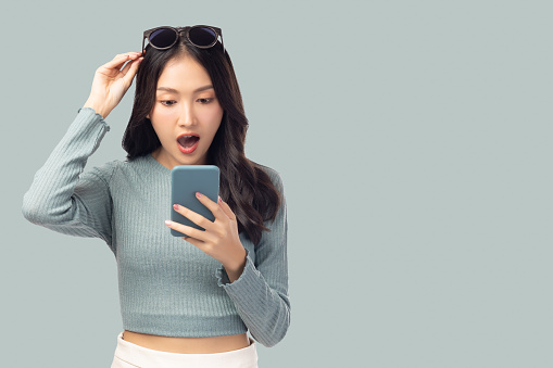 Happy and excited young woman using mobile phone standing over isolated on green background and copy space Young girl using smartphone for shopping online chat and texting message She get surprised