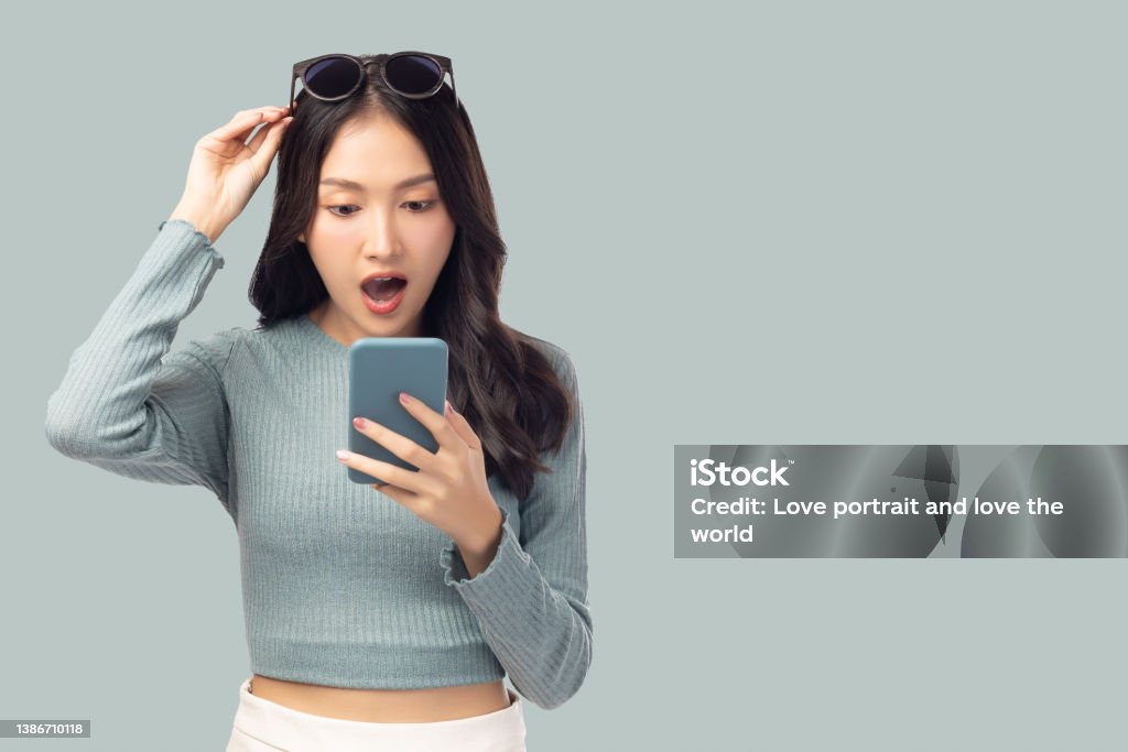 Happy and excited young woman using mobile phone standing over isolated on green background and copy space Young girl using smartphone for shopping online chat and texting message She get surprised Asia Stock Photo