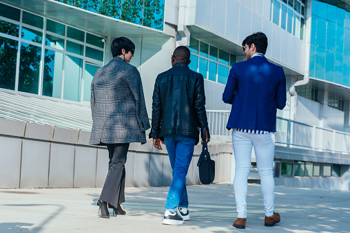 Full-length rear view of formally dressed colleagues talking while walking outside their offices