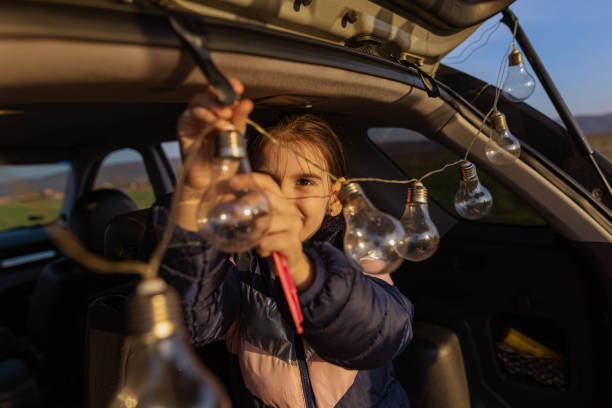 Cheerful Caucasian girl adjsting the light bulb into car trunk, during car camping stock photo