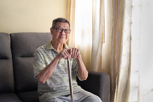 Portrait of a senior man sitting and holding a walking stick at home.