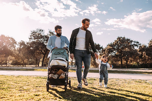 Male gay couple walking with their little daughter in the park at sunset. Modern family concept.