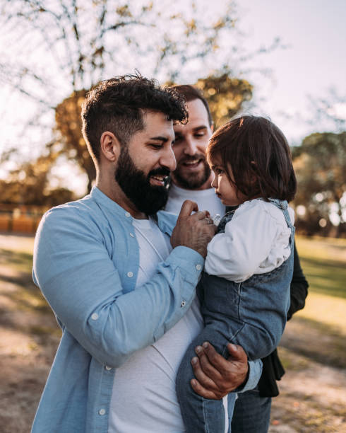 Happy male gay couple with their daughter in their arms. Her father gives her the pacifier. Happy male gay couple with their daughter in their arms. Her father gives her the pacifier. common couple men outdoors stock pictures, royalty-free photos & images