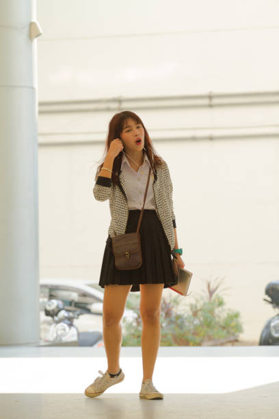 The teen Asian girl with university uniform standing on the pink background.