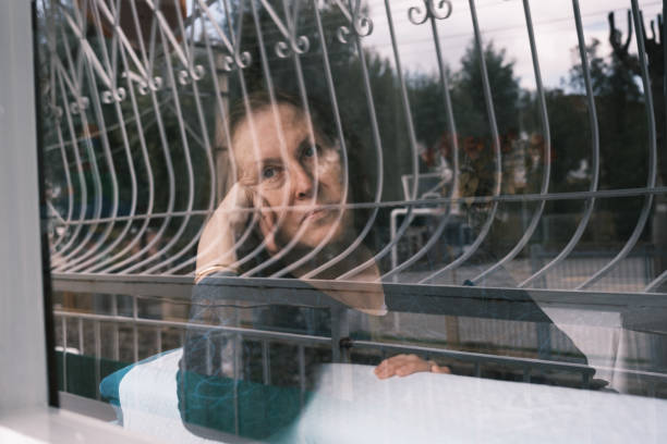 istock Lonely senior woman watching out the window 1386717020
