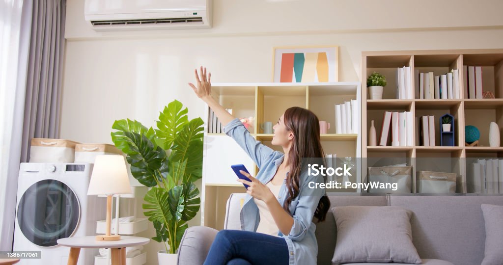 IOT smart home concept IOT smart home system concept - asian young woman using app on mobile phone to turn on air conditioner in living room Air Conditioner Stock Photo