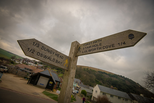 A wooden sign indicates distances and footpaths beneath a cloudy sky.