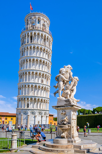 The Putti Fountain and the Leaning Tower are two of the landmarks of the Piazza dei Miracoli in Pisa, formally known as Piazza del Duomo, the iconic artistic center of the city, listed as a UNESCO World Heritage Site since 1987. Tourists visiting.